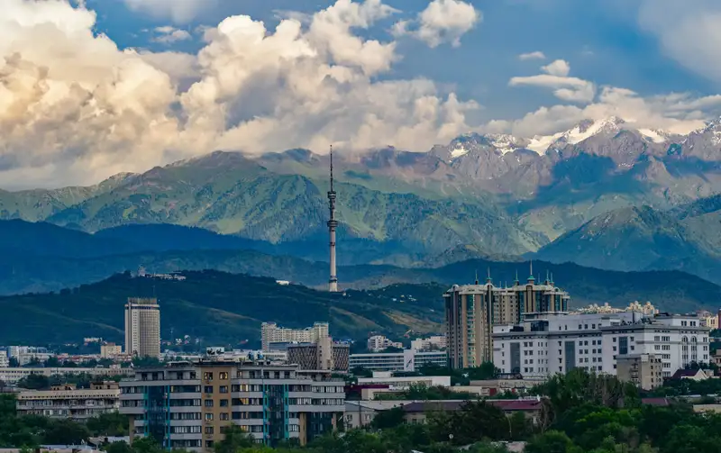 Almaty city skyline with its television tower, backed by the green slopes and snow-capped peaks of the Trans-Ili Alatau